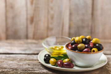 Green, black and red olives, olive oil on a brown wooden background. Fresh juicy olives in a bowl and fresh olive leaves. Vegan. Olive fruits. Place for text. Copy space.