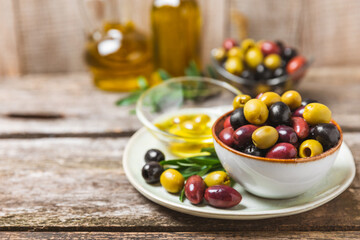 Green, black and red olives, olive oil on a brown wooden background. Fresh juicy olives in a bowl and fresh olive leaves. Vegan. Olive fruits. Place for text. Copy space.