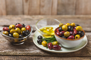 Green, black and red olives, olive oil on a brown wooden background. Fresh juicy olives in a bowl and fresh olive leaves. Vegan. Olive fruits. Place for text. Copy space.