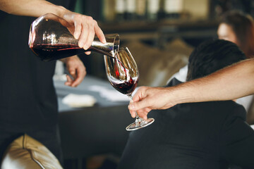 Sommelier school. Professional wine waiter pouring wine into decanter to the glasses during...