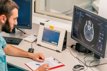 Concentrated male physician sits at a computer monitor in a room for describing MRI images and...