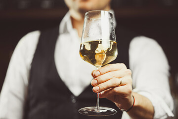 Bartender at the bar hands the camera a glass of white wine, close-up.