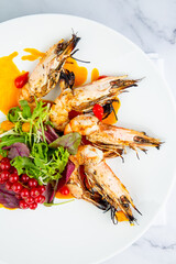  cooked shrimp with herbs and berries on a white plate, side view