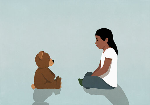 Girl sitting and staring at teddy bear on blue background
