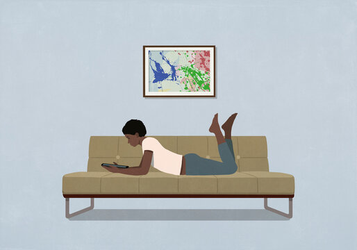 Woman laying and relaxing, using digital tablet on living room sofa at home
