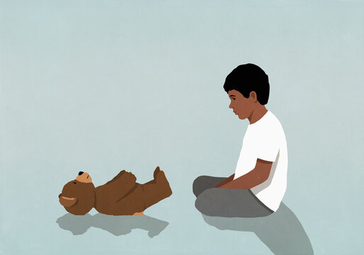 Curious boy sitting and watching teddy bear on back
