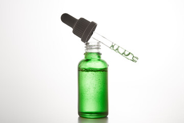 Black cap with pipette lies on open green glass bottle.