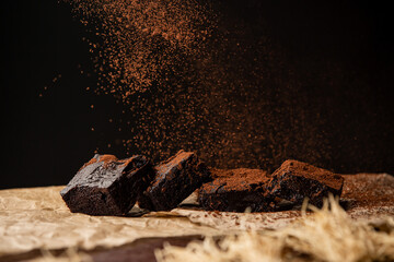 Delicious chocolate brownies on baking parchment paper sprinkled with cocoa powder over black...