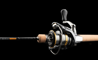 Fishing rod spinning with the line close-up. Fishing rod and reel isolated on black background....
