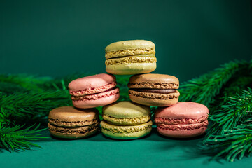 colorful macaroons on a table and on a green background among the branches of a Christmas tree
