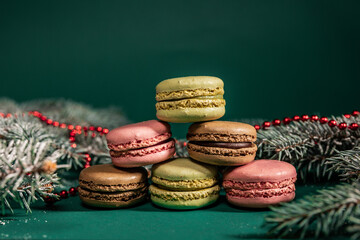 colorful macaroons on a table and on a green background among the branches of a Christmas tree