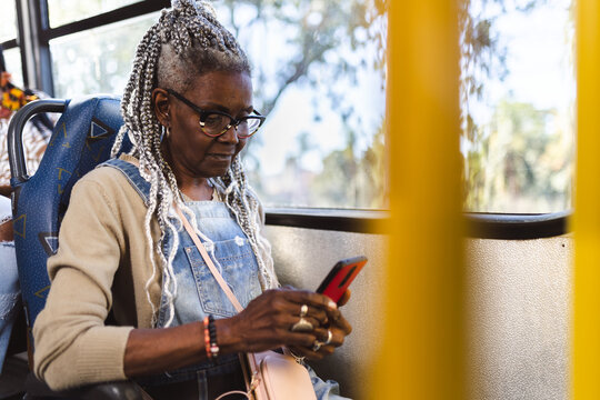 Stylish retired woman on the bus typing message using smartphone.
