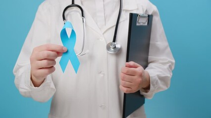 Close up of unrecognizable woman doctor in white uniform with stethoscope holding blue ribbon awareness. Men's health and Prostate cancer awareness campaign in November month. Symbol of medical issues