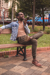 Young black man, sitting on the bench in the square, talking on his smartphone.