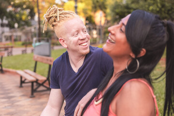 Cheerful interracial couple sitting on the bench in the square on a sunny day.