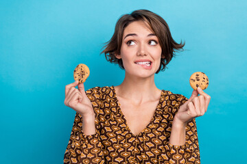 Photo of cute cheerful minded person biting lips arms hold cookies look empty space isolated on...