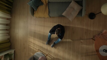Top view of a man sitting on the living room floor. A depressed man hiding his face in the palms of...
