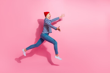Fototapeta na wymiar Full length photo of positive excited girl dressed striped shirt jumping high catching arms empty space isolated pink color background