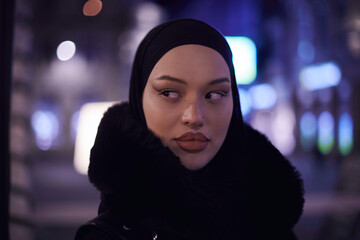 Muslim woman walking on an urban city street on a cold winter night wearing hijab