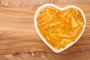 Capsules with Vitamin D, E or Omega 3,6,9 fatty acids in heart shape bowl on old wooden backgrounds. Food supplement oil filled fish oil. Natural supplements for healthy good life concept. Banner.