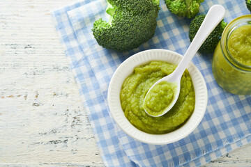 Green broccoli baby food in white bowl and jar on table. Green baby food. Child first feeding...