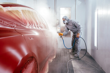 Automotive paint services, quality auto body shop concept. Painting the car in red color in the...