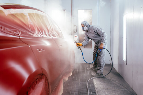 Automotive paint services, quality auto body shop concept. Painting the car in red color in the paint chamber on the service.