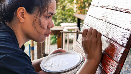 Close-up of Asian woman painter creating art use a paintbrush to draw lettering designs on a wooden...