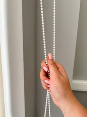 A female hand holding a beaded chain for the blinds