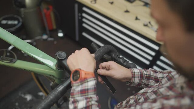 Bicycle mechanic changing new tape on handlebars of cycle in workshop. Concept of bike repair and service. Bicycle technician fitting tape on handlebar. Bike repairman at work in repair shop. 