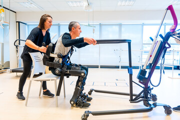 Mechanical exoskeleton. Physiotherapy assistant lifting disabled person with robotic skeleton to...
