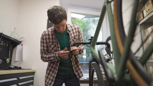 Bicycle mechanic changing new tape on handlebars of cycle in workshop. Concept of bike repair and service. Bicycle technician fitting tape on handlebar. Bike repairman at work in repair shop. 