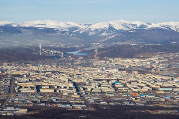 Top view of the city of Magadan. A large northern city in a valley among the mountains. Many buildings. Snow-capped mountains in the distance. Magadan, Magadan region, Russian Far East.