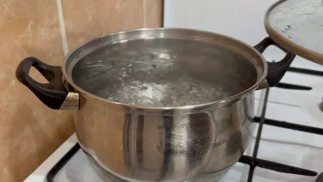 a woman removes a glass lid from a pot in which water is boiling, cooking hitting the camera