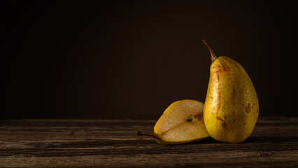 one and a half ripe pears lie on a plank table against the background of a dark wall with a light spot. side view. moody artistic photo with copy space