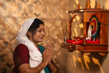 devotional Indian woman praying to god during early morning sunrise near mandapam at home - concept of religious rituals, traditional custom and spirituality