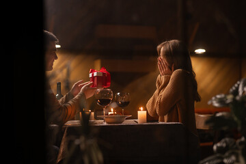 Romantic dinner for two at home, a man gives a woman a gift for a birthday or valentine's day, a couple in love in the evening, sitting at a table with candles, concept of holiday gift