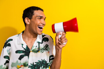 Photo of eccentric man with piercing dressed palm print shirt scream in loudspeaker at empty space isolated on yellow color background
