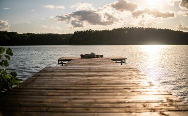 Stunning view of a tranquil lake with a wooden dock silhouetted against the sky at sunset.