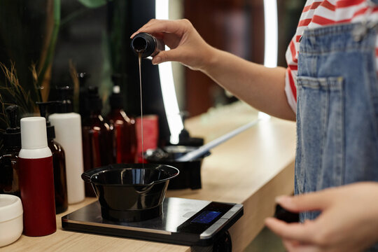 Side view closeup of hairstylist pouring developer into plastic bowl and mixing hair dye solution, copy space - Powered by Adobe