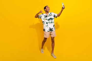 Fototapeta na wymiar Full length photo of nice young male showing thumb up selfie walk wear trendy palms print garment isolated on yellow color background