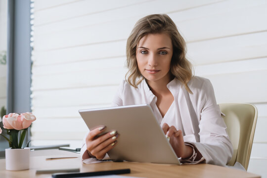 girl works in the office. blonde woman doing work on a tablet in her office, white wall in the background. business business work in an office building concept
