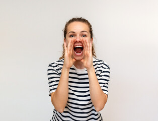 Woman wearing striped t-shirt shouts loudly cupping hands around her mouth. Scream and shout.