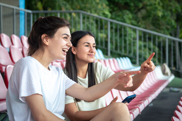 Slim young women in sportswear sitting on stadium seats.