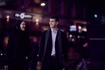Happy multicultural business couple walking together outdoors in an urban city street at night near...