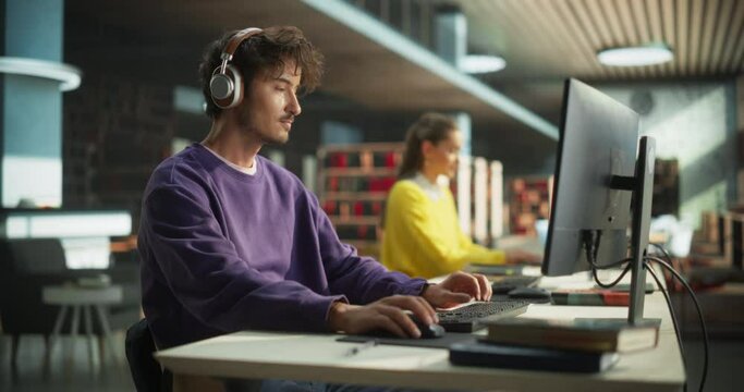 Excited Young Male is Focused on Creating a College Presentation for Class Assignment, Using Online Office Software on Desktop Computer in a Public Library Space with Other Students