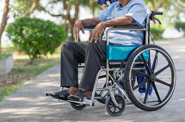 Cropped image of elderly man sits in a wheelchair outdoors in nature.
