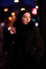 Muslim woman walking on an urban city street on a cold winter night wearing hijab