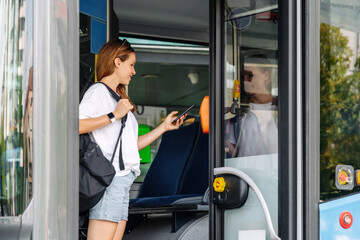 Urban woman passenger of public transportation pays bus with her mobile phone and contactless...