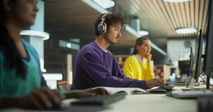Portrait of a Smart Male Working on a Computer with a Group of University Students. Young Man Wearing Headphones, Doing Homework Assignment and Preparing for STEM Exams in a College Library